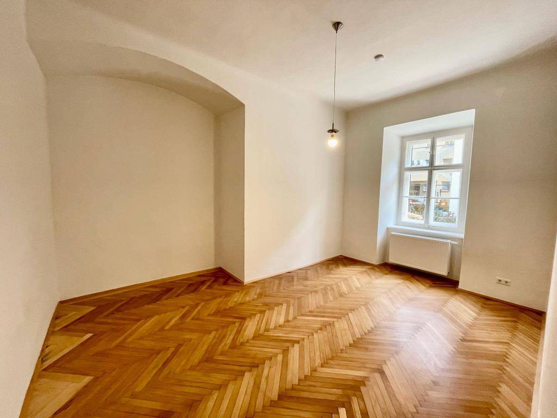 Lichtdurchfluteter Raum mit elegantem Fischgrätparkett, Bogenarchitektur und Fenster.