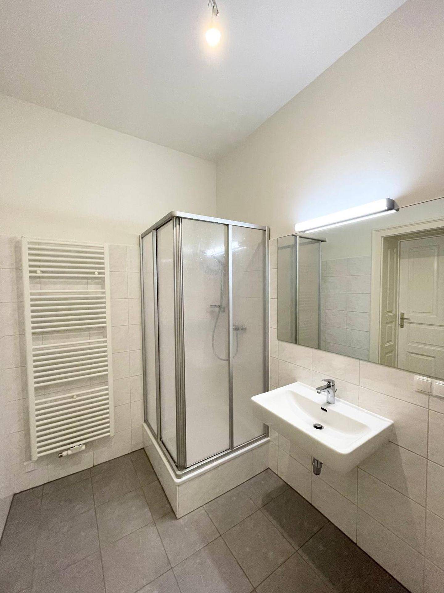 Modernes Badezimmer mit Duschkabine, Waschbecken, Spiegel und beheiztem Handtuchhalter.