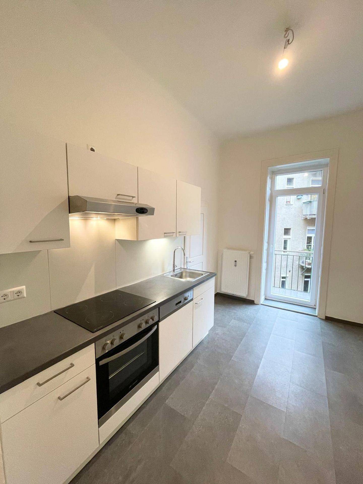 Moderne Küche mit weißen Schränken, integrierten Geräten und Zugang zu einem französischen Balkon.