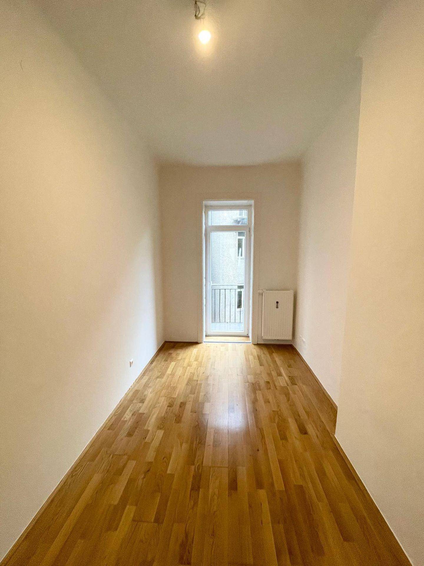 Helles Zimmer mit Holzboden und Zugang zu einem französischen Balkon, ideal für ein Schlafzimmer.