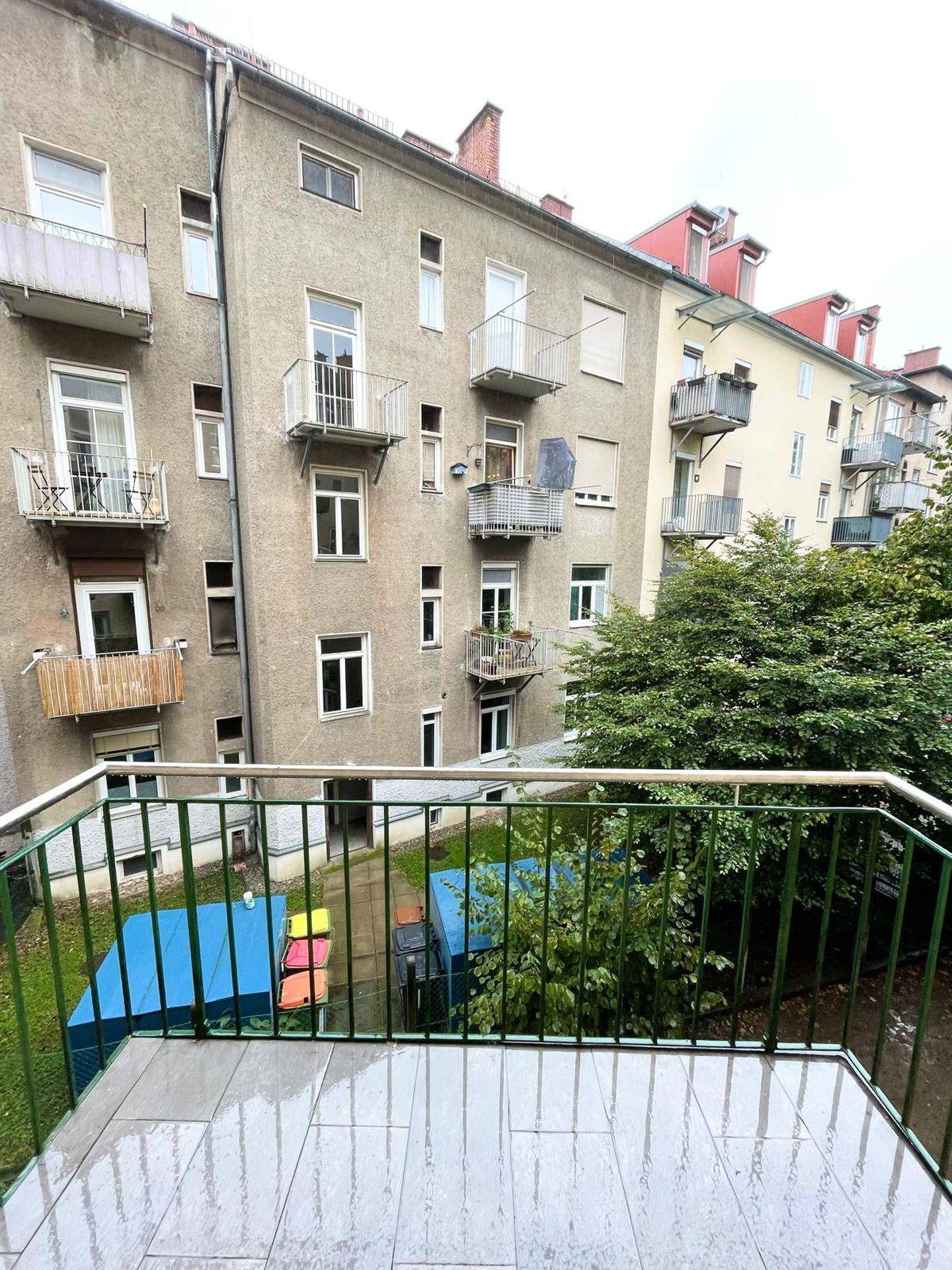 Balkon mit Blick auf den Innenhof und umliegende Gebäude, ausgestattet mit Fliesenboden und Metallgeländer.
