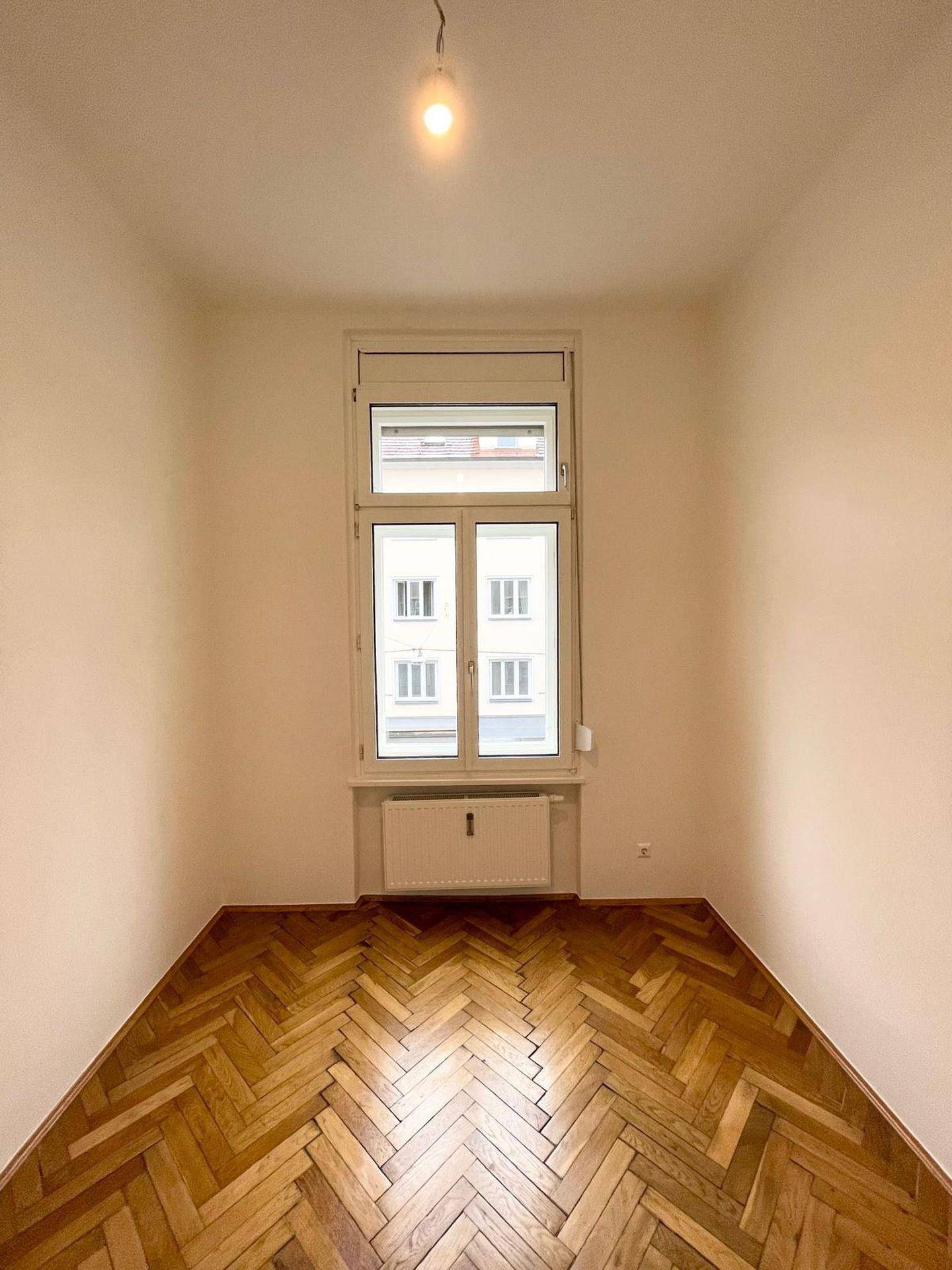 Gemütliches Zimmer mit Fischgrätparkett und einem großen Fenster, gut geeignet als Schlaf- oder Arbeitszimmer.
