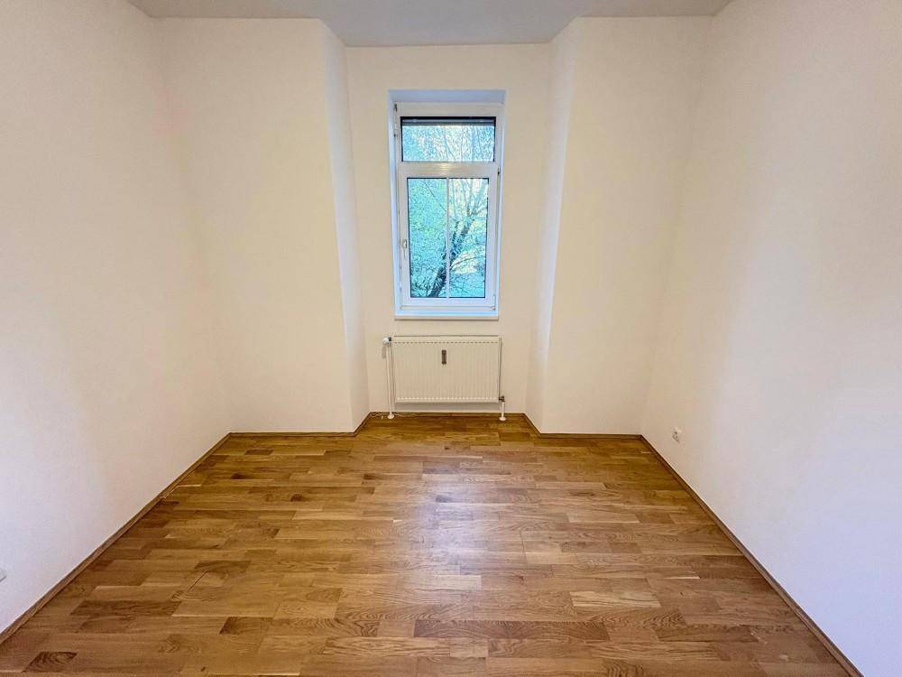 Helles Zimmer mit Parkettboden und einem Fenster, bietet vielseitige Nutzungsmöglichkeiten.