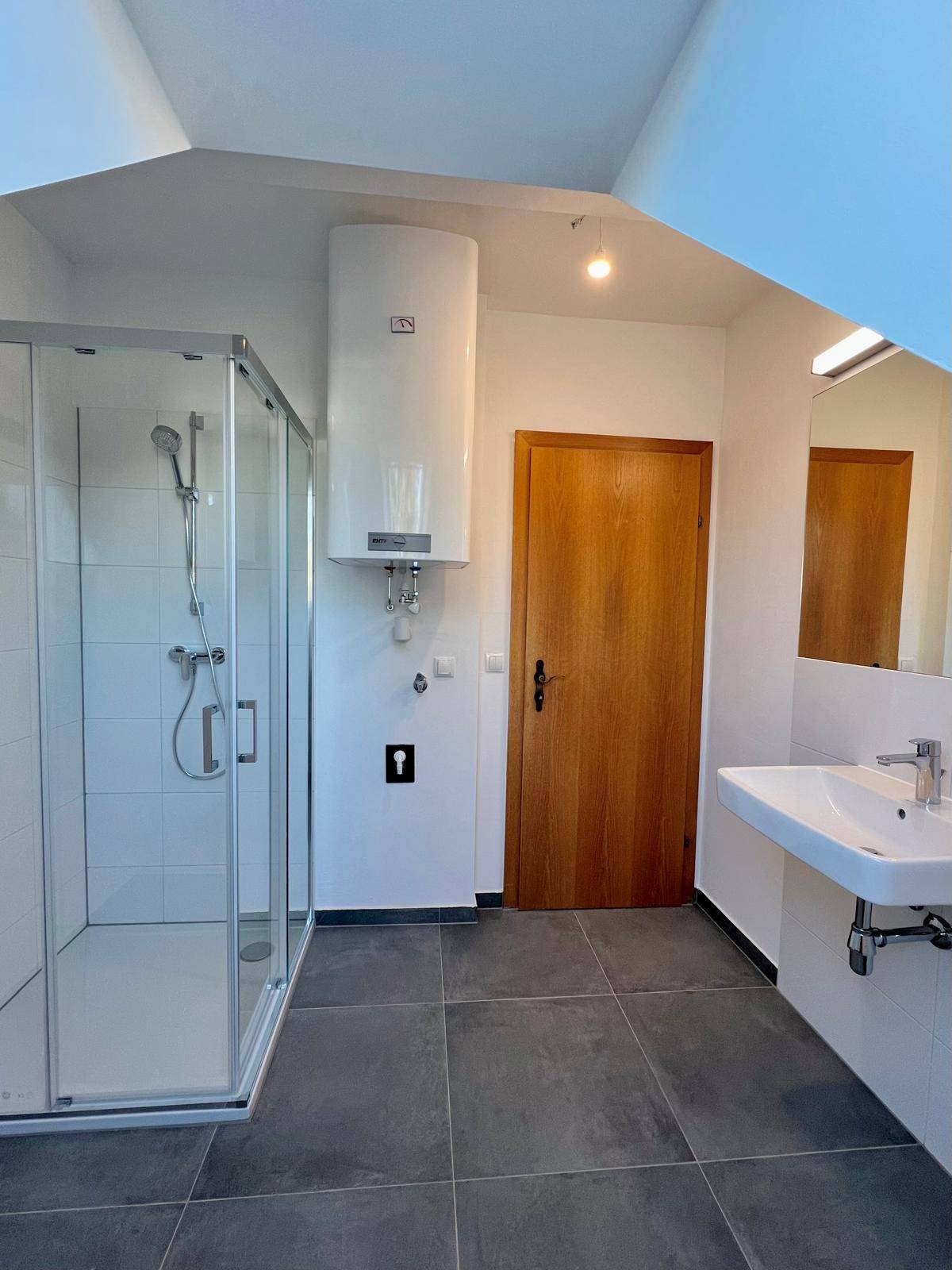 Modernes Badezimmer mit Duschkabine, Waschbecken und dunklen Bodenfliesen.