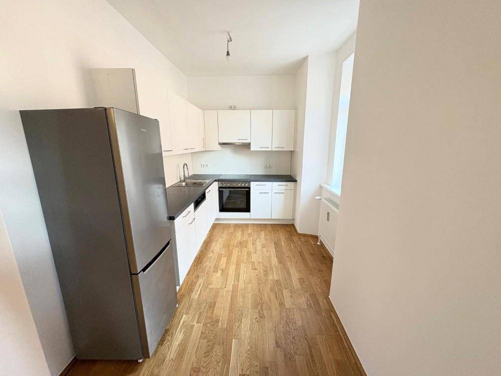 Moderne Küche mit weißen Schränken, dunkler Arbeitsplatte und großem Kühlschrank.