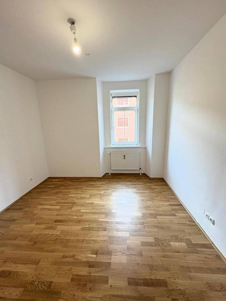 Geräumiges Zimmer mit Parkettboden und Fenster, ideal für Wohn- oder Essbereich.