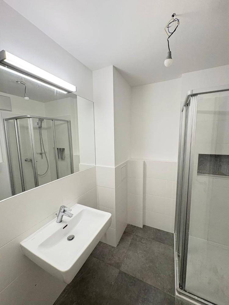 Modernes Badezimmer mit Waschbecken, Spiegel und Duschkabine, hell gefliest.