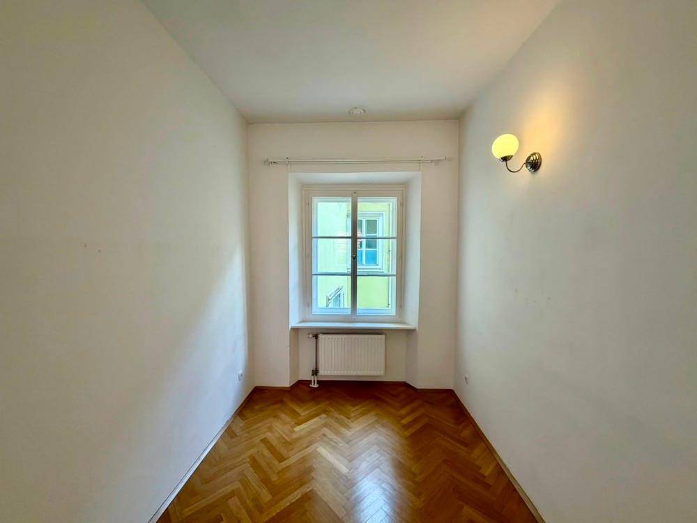 Kleiner, heller Raum mit Fischgrätparkettboden und einem Fenster, ausgestattet mit einer Wandleuchte.