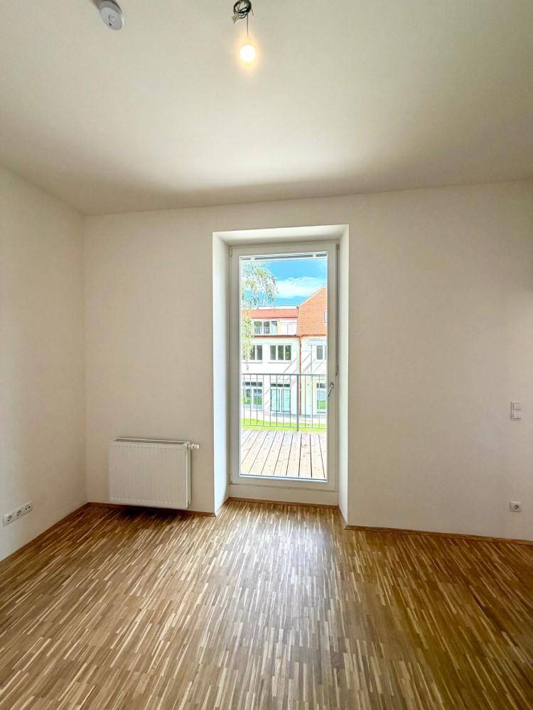 Heller Raum mit Holzfußboden und Zugang zu einem Balkon, ideal für Wohnzwecke.