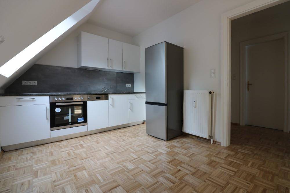 Moderne Küche im Dachgeschoss mit weißen Schränken, Einbaugeräten und schräger Decke.