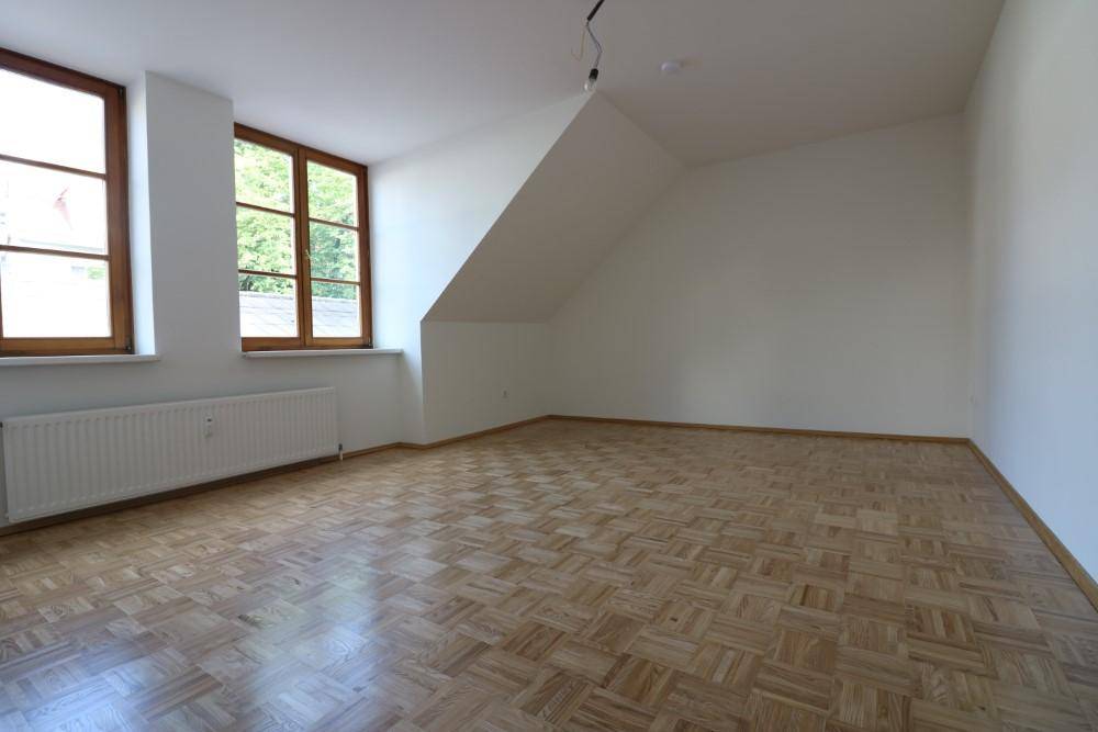 Heller Raum im Dachgeschoss mit Parkettboden, schrägen Wänden und Blick ins Grüne.