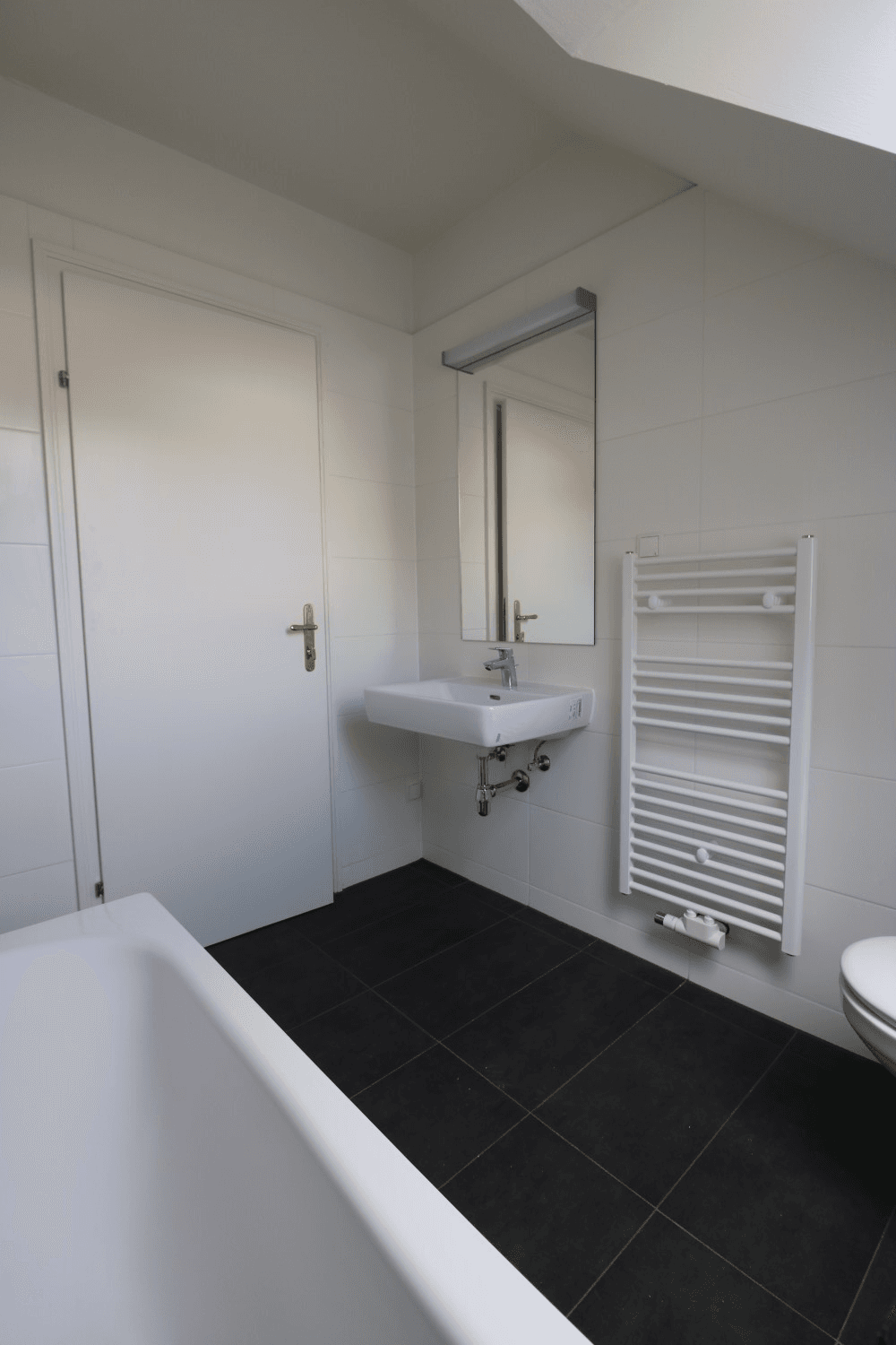 Modernes Badezimmer mit Badewanne, Waschbecken, Spiegel und beheiztem Handtuchhalter.