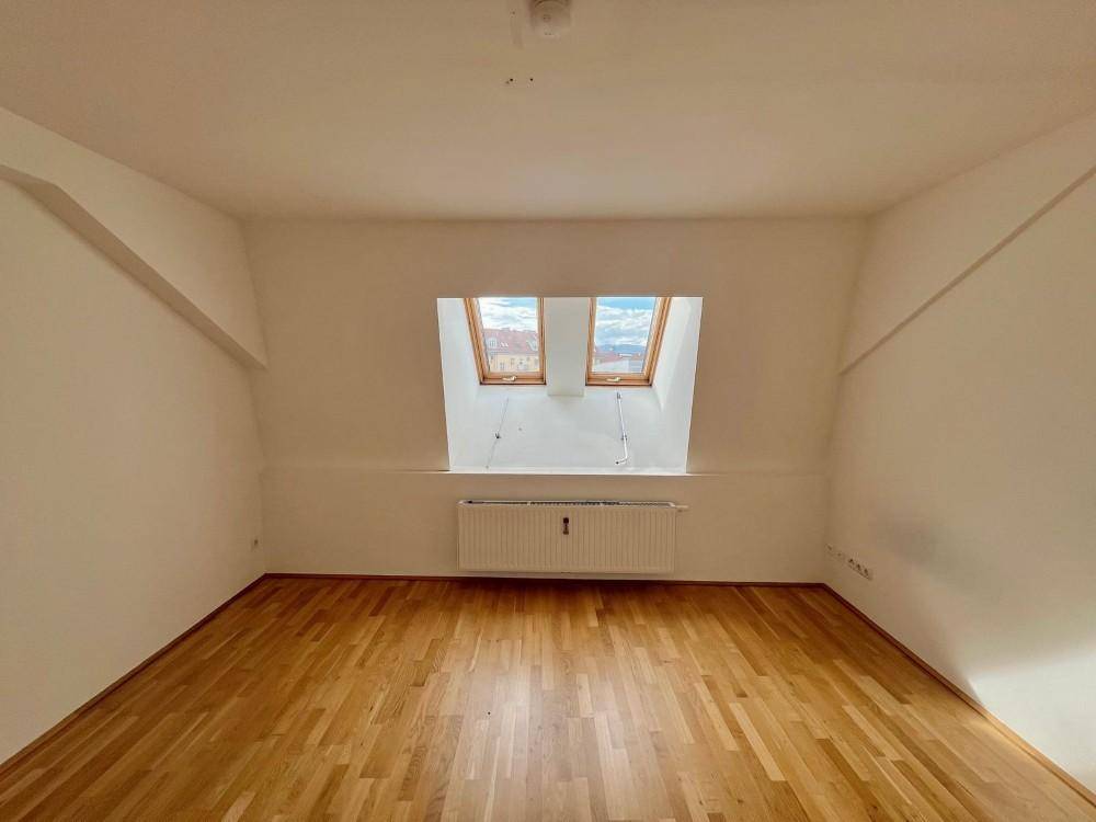 Geräumiges Zimmer im Dachgeschoss mit Holzboden und zwei Dachfenstern, bietet viel Tageslicht.
