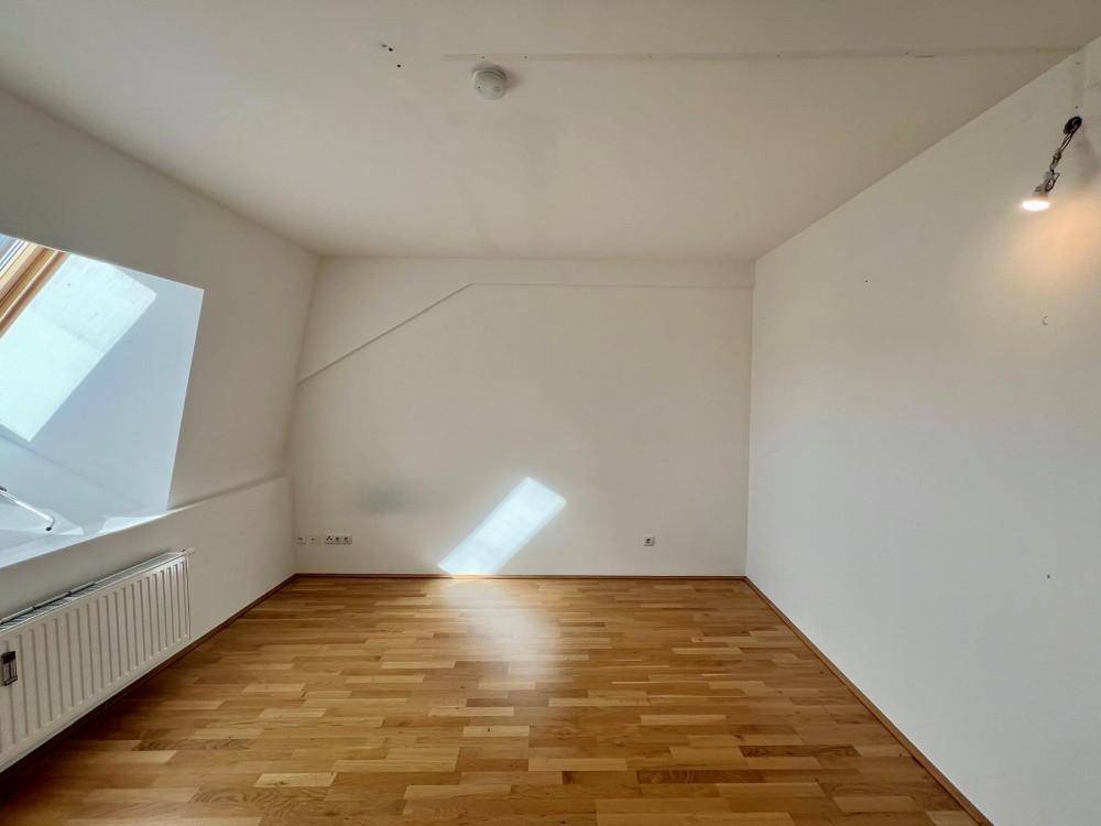Helles Zimmer mit Holzboden und schrägen Wänden im Dachgeschoss, gut beleuchtet durch ein Dachfenster.