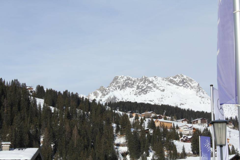 Idyllisches Bergdorf mit verschneiten Dächern und dichten Nadelwäldern vor majestätischer Bergkulisse.
