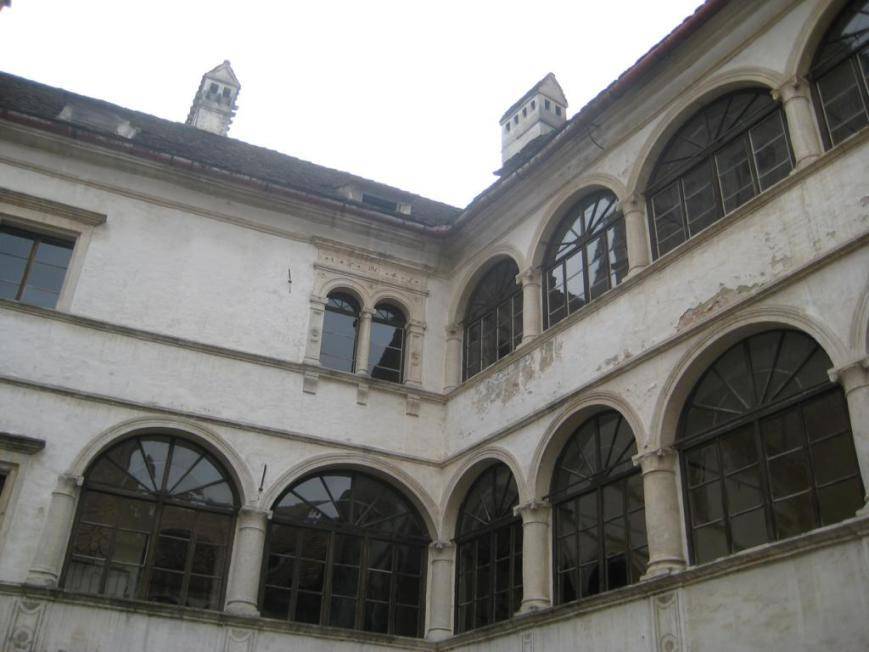 Historischer Innenhof mit vielen großen Rundbogenfenstern und weiß getünchten Wänden.