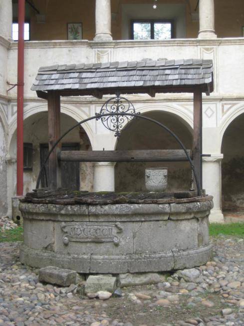 Historischer Brunnen mit Holzdach und Steinmauerwerk im gepflasterten Innenhof des Anwesens.