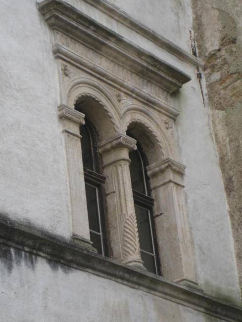 Detail eines kunstvoll verzierten Fensters mit Steinsäulen und historischer Architektur an der Fassade.