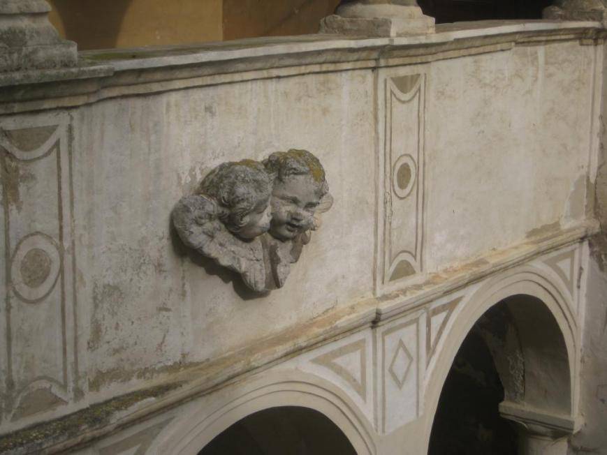 Dekorative Putten-Skulpturen an einer historischen Wand mit Rundbögen und geometrischen Mustern.