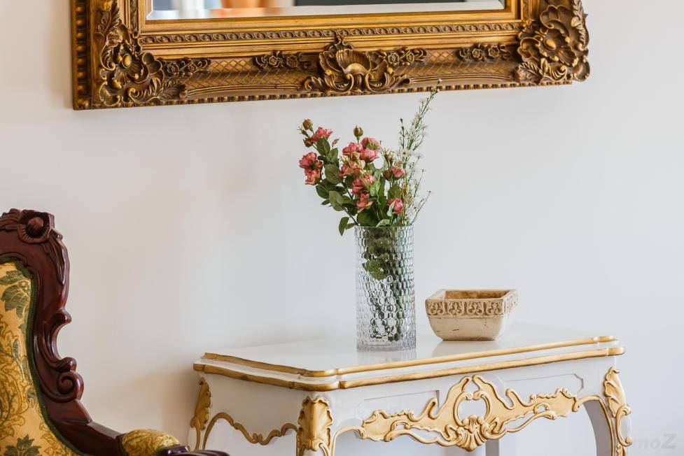 Detailaufnahme eines eleganten Konsolentisches mit Blumen und einem verzierten Stuhl in einem Innenraum.