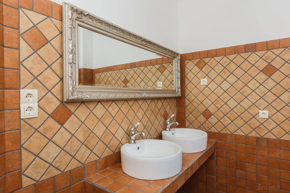 Badezimmer mit zwei Aufsatzwaschbecken, großem Spiegel und rustikalen Terrakotta-Fliesen an den Wänden.