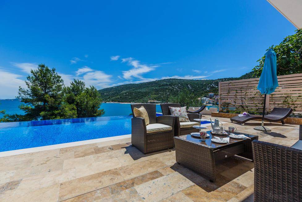 Große Sonnenterrasse mit Infinity-Pool, Lounge-Möbeln und weitem Meerblick unter strahlendem Himmel.