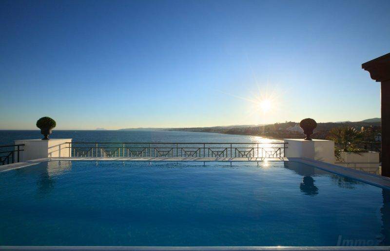 Infinity-Pool mit spektakulärem Meerblick und strahlendem Sonnenschein über dem Horizont.