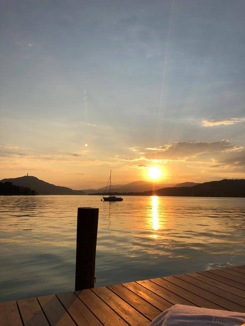Spektakulärer Sonnenuntergang über dem See, gesehen von einem Holzsteg mit Segelboot.