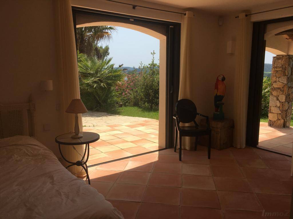 Helles Schlafzimmer mit Terrakottafliesen und direktem Zugang zu einer Außenterrasse mit Gartenblick.