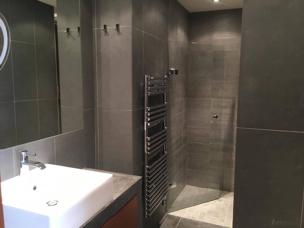 Modernes Badezimmer mit grauen Fliesen, ebenerdiger Dusche und beheiztem Handtuchhalter.