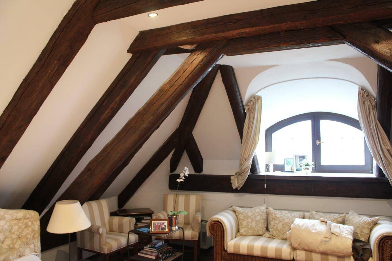 Gemütliches Wohnzimmer mit sichtbaren Holzbalken, Dachschräge und einem charmanten Bogenfenster.