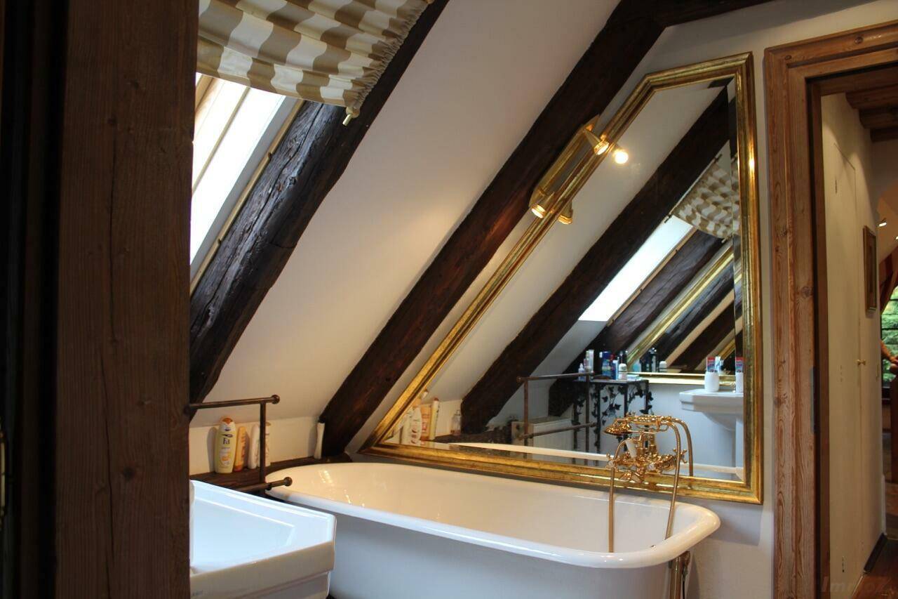 Elegantes Badezimmer mit freistehender Badewanne, großem Spiegel und sichtbaren Holzbalken unter der Dachschräge.
