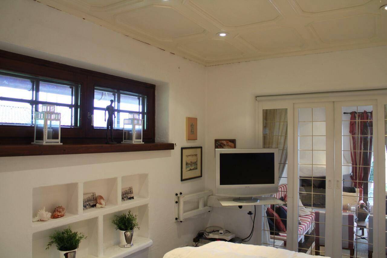 Helles Schlafzimmer mit eingebauten Regalen, Fernseher und Zugang zu einem weiteren Wohnbereich.