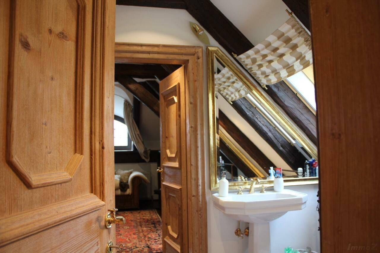 Rustikales Badezimmer mit Holzdetails, Waschtisch und Spiegel, der die Dachschräge reflektiert.