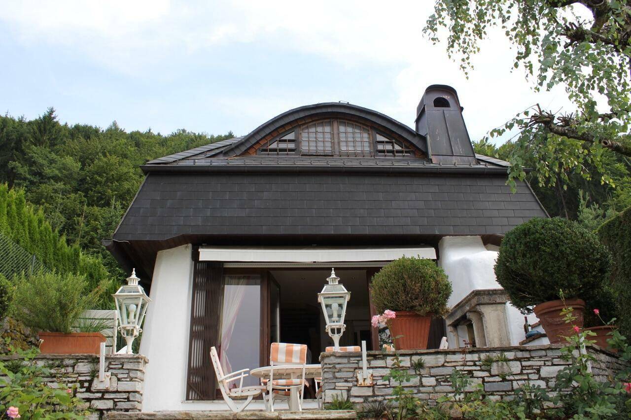 Charmante Terrasse mit Steinmauern und Gartenmöbeln vor einem Haus mit besonderem Dachfenster.