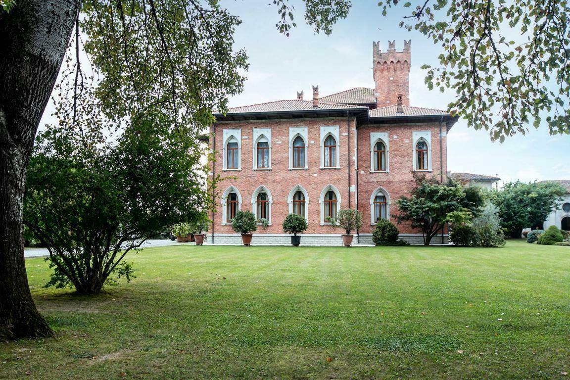Elegante Ziegelfassade der Villa mit hohen Bogenfenstern und weitläufigem Rasen, umgeben von altem Baumbestand.