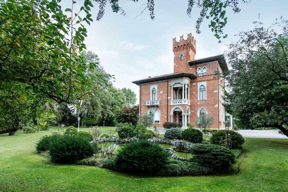 Historische Villa mit Ziegelfassade, umgeben von einem gepflegten Garten mit dekorativem Teich und Springbrunnen.