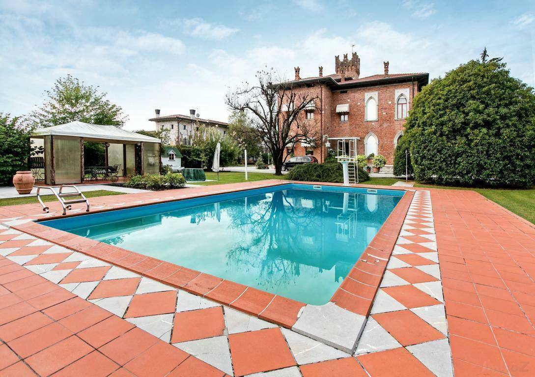 Großer Außenpool mit gefliestem Rand und Sprungbrett, im Hintergrund die historische Villa und ein Gartenpavillon.