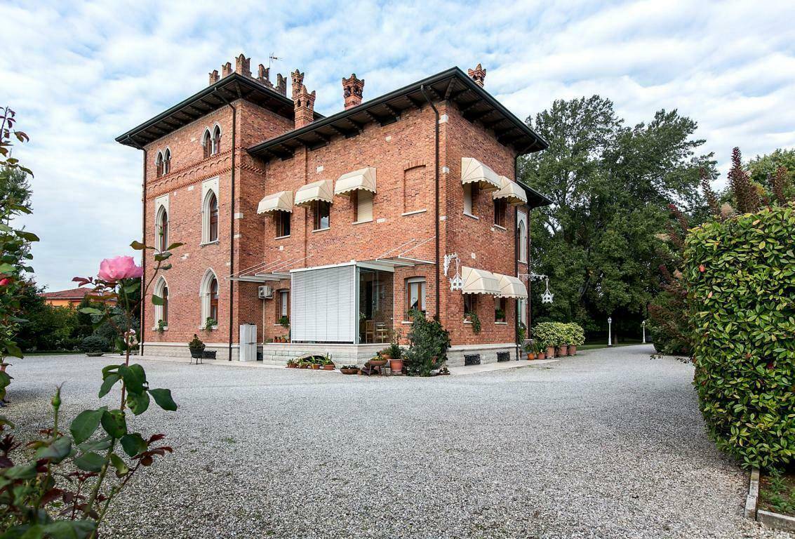 Seitenansicht der historischen Villa mit Ziegelfassade, Markisen und einem Wintergarten, umgeben von einem gepflegten Garten.