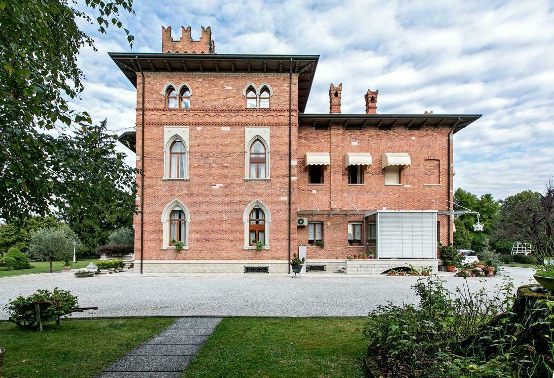 Seitenansicht der historischen Villa mit Ziegelfassade, Markisen und einem Wintergarten, umgeben von einem gepflegten Garten.