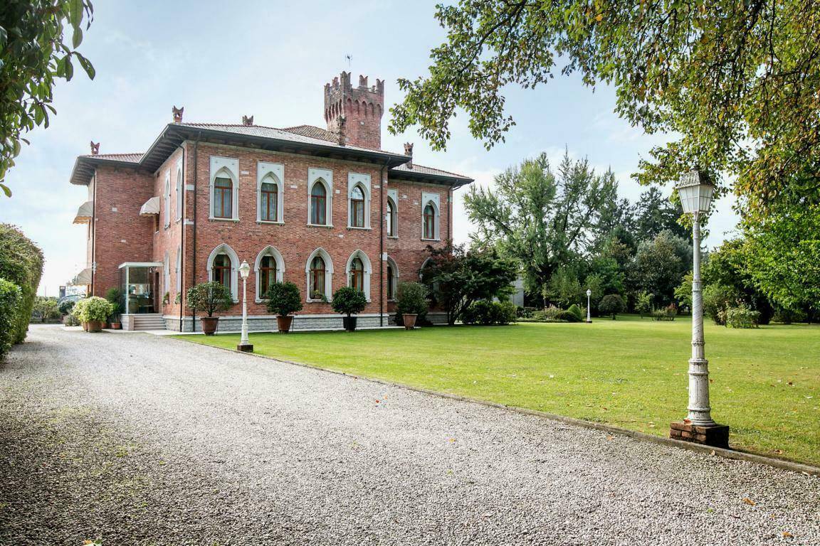 Elegante Ziegelfassade der Villa mit hohen Bogenfenstern und gepflegter Kiesauffahrt, umgeben von Grünflächen.