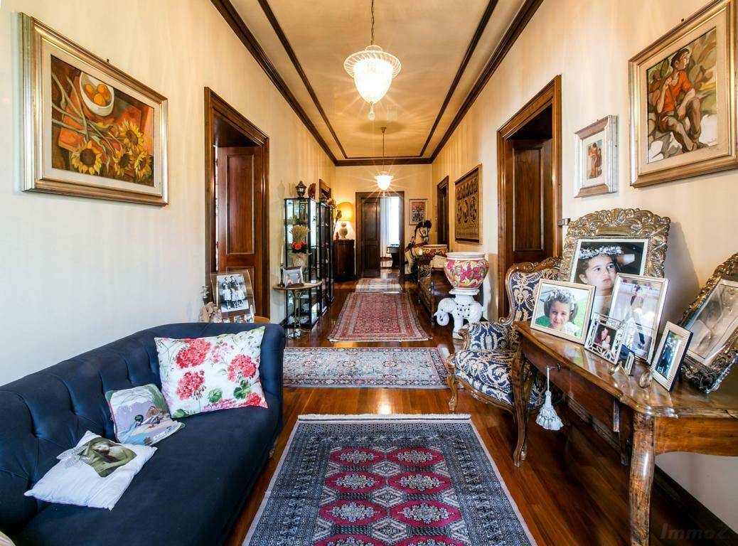 Langer, eleganter Flur mit Holzboden, Teppichen und antiken Möbeln, geschmückt mit Kunstwerken und Familienfotos.
