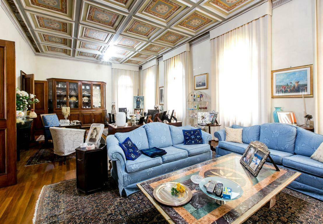 Geräumiges Wohnzimmer mit blauen Sofas, Holzboden und einer reich verzierten Kassettendecke, ideal für gesellige Stunden.