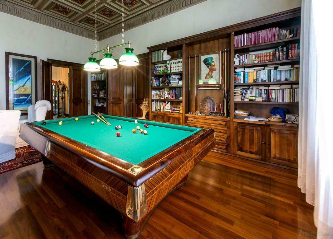Elegantes Spielzimmer mit Billardtisch, Holzboden und eingebauten Bücherregalen, unter einer kunstvoll bemalten Kassettendecke.