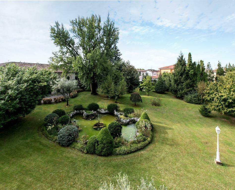 Vogelperspektive auf den weitläufigen Garten mit einem großen Teich, umgeben von altem Baumbestand und Rasenflächen.