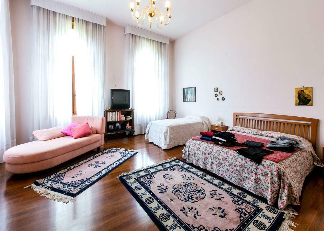 Helles Schlafzimmer mit Holzboden, zwei Betten und einem rosa Chaiselongue, durchflutet von natürlichem Licht.