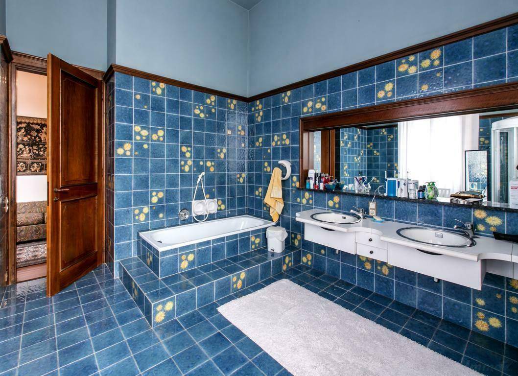 Badezimmer mit blauen Fliesen und gelben Akzenten, ausgestattet mit einer Badewanne und einem Doppelwaschbecken.