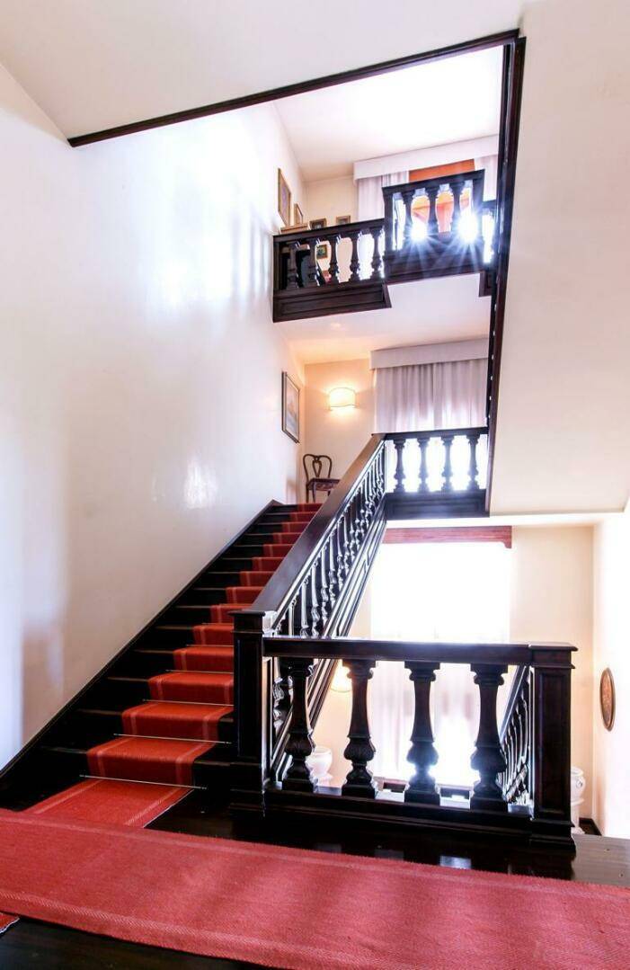 Elegante Holztreppe mit rotem Teppichläufer und kunstvollen Balustern, die die oberen Etagen der Villa verbindet.