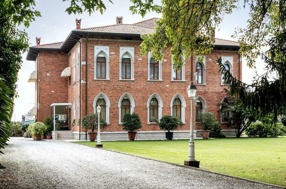 Elegante Ziegelfassade der Villa mit hohen Bogenfenstern und gepflegter Kiesauffahrt, umgeben von Grünflächen.