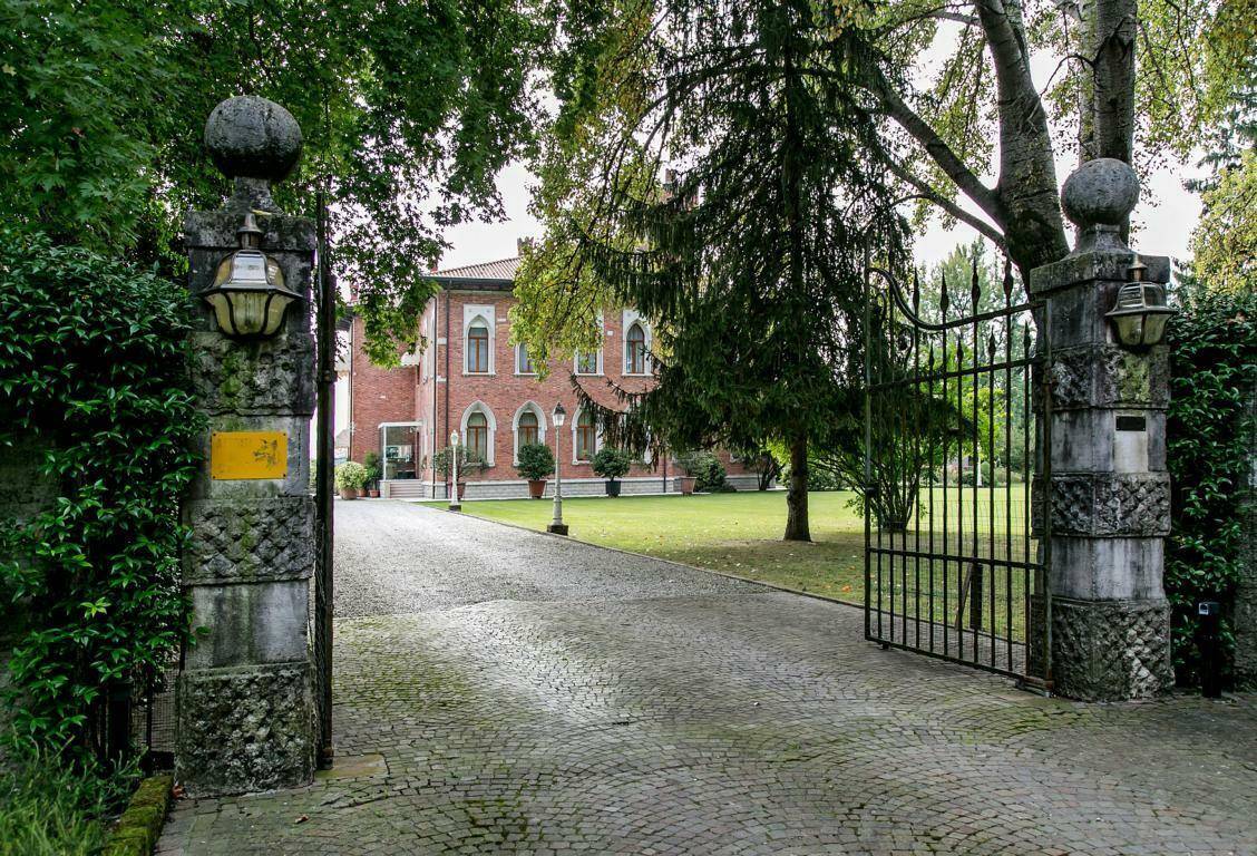 Repräsentatives Eingangstor aus Stein und Schmiedeeisen, das zu einer gepflasterten Auffahrt und der historischen Villa führt.